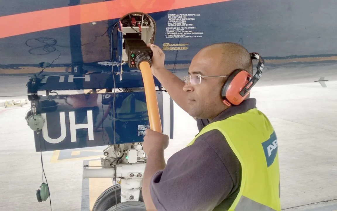 Technician with hearing protection connecting ground support equipment to an aircraft fuselage