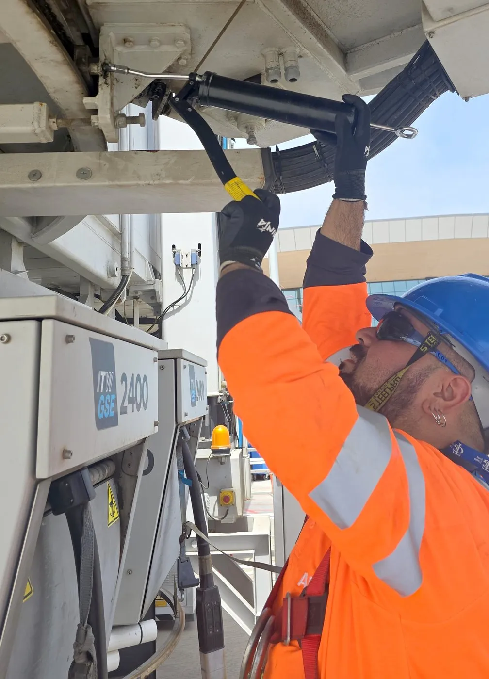 APS LATAM technician working on equipment under a boarding bridge on the apron